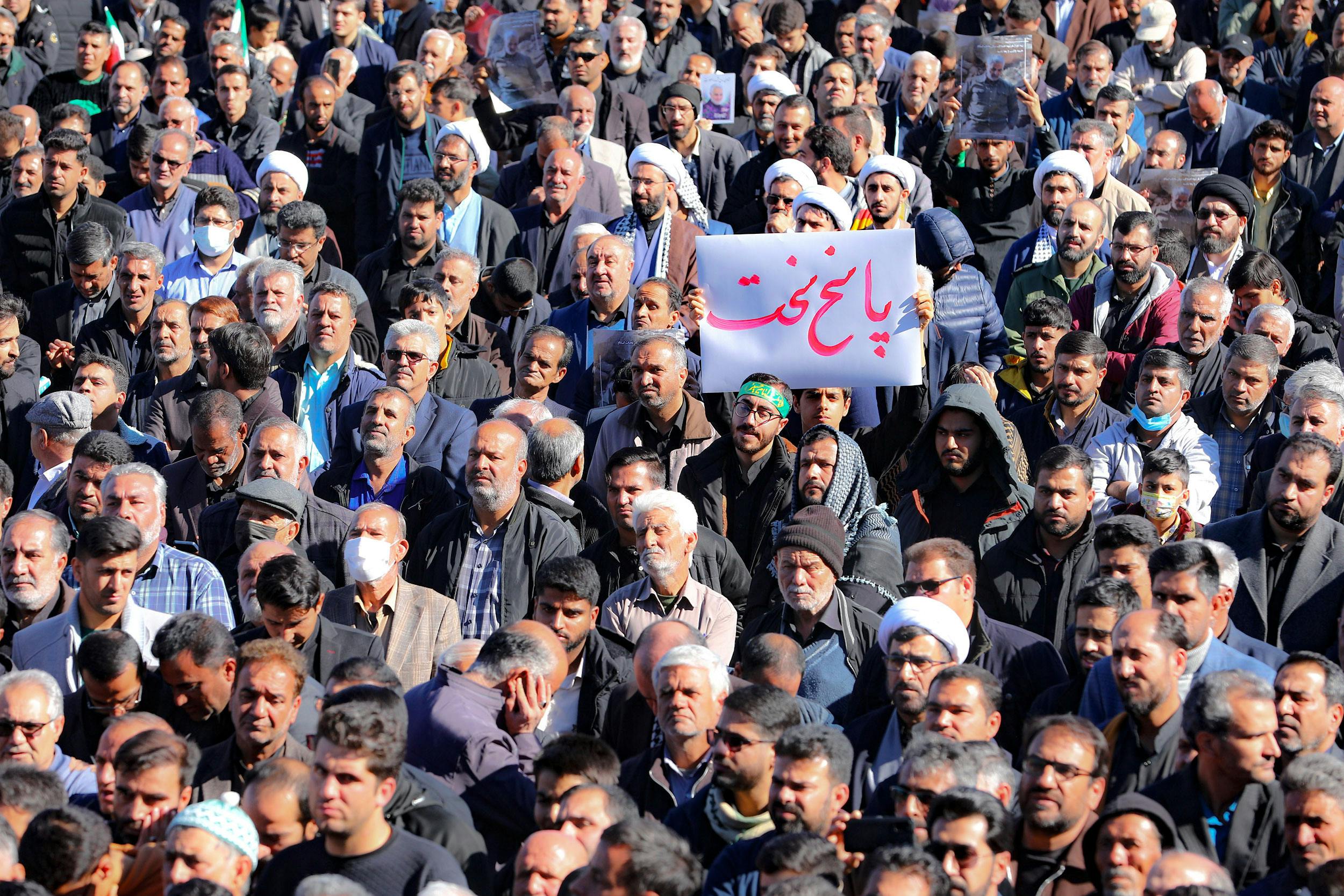 تجمع در مراسم تشییع کشتگان انفجارهای کرمان. یک نفر یک برگ کاغذ بالا گرفته که روی آن نوشته: پاسخ سخت