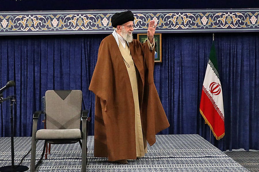علی خامنه‌ای، رهبر جمهوری اسلامی با لبخند دست خود را بلند کرده و به حاضران ابراز احساسات می‌کند.