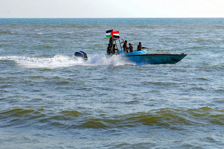 چند سرباز گارد ساحلی یمن وابسته به حوثی‌ها سوار با قایق گشت‌زنی با پرچم‌های یمن و فلسطین در دریای سرخ در حال گشت‌زنی هستند.