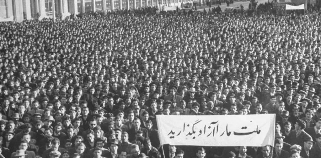 عکس سیاه و سفید از جمعیت انبوه مردم. در جلوی عکس، یک بنر سفیدرنگ بالا گرفته‌اند که روی آن نوشته: ملت ما را آزاد بگذارید