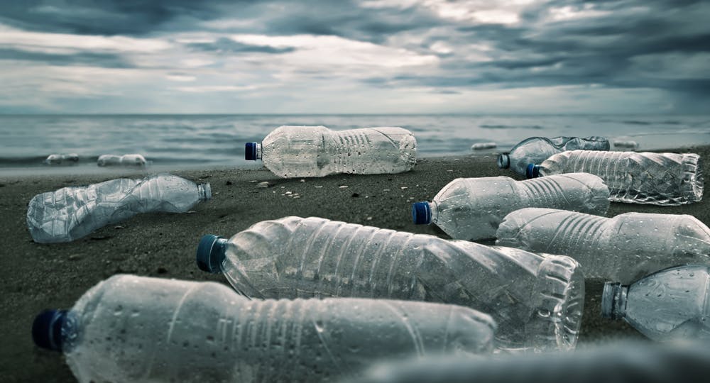 تصویر تزئینی از شاتر استاک چند بطری پلاستیکی آب را رها شده در یک ساحل نشان می‌دهد.