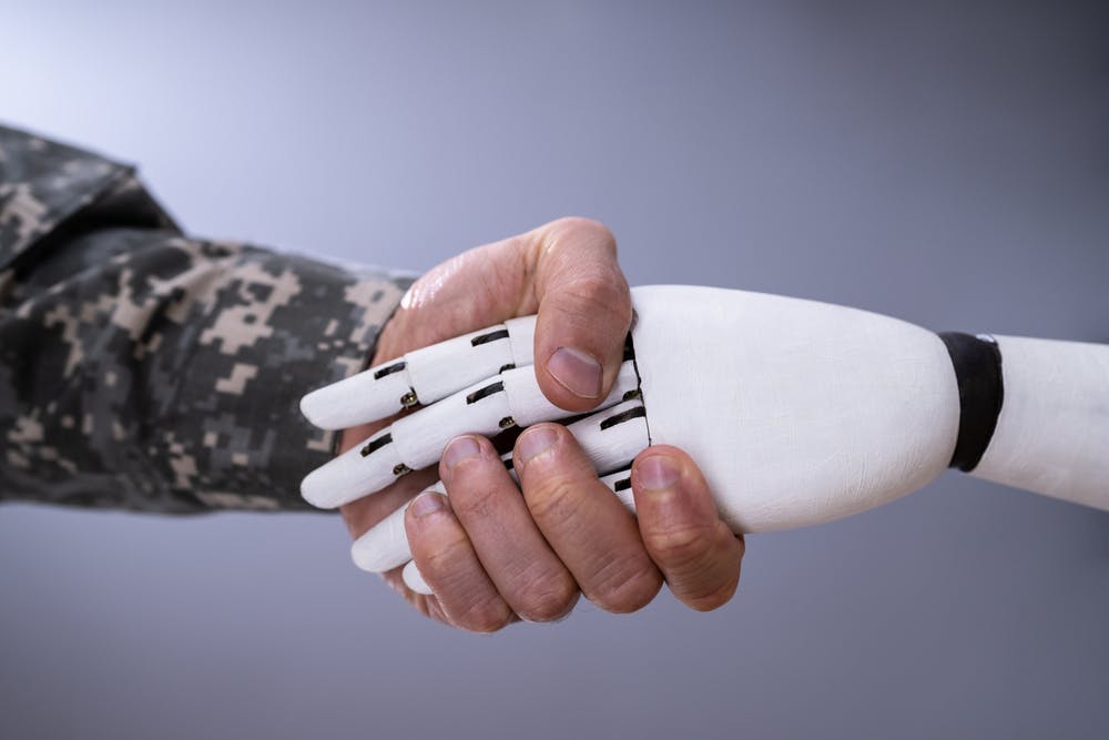 طرحی از یک دست ربات و یک دست انسان با پیرهن نظامی در حال دست دادن با یکدیگر
