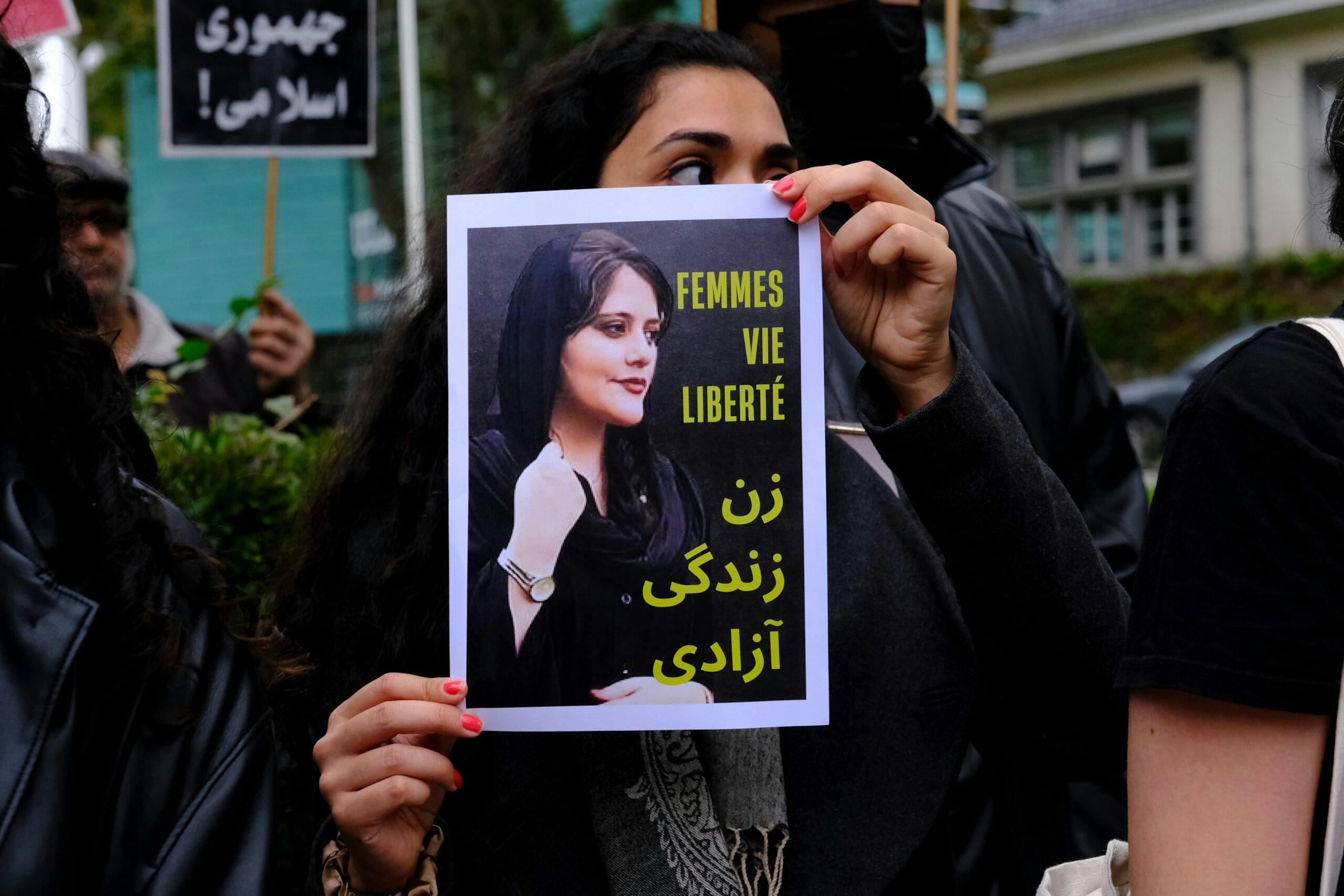 تصویر تزئینی از یک راهپیمایی جنبش زن، زندگی، آزادی. یک زن صفحه‌ای پرینت شده با همین شعار را در دست دارد و پشت سر او یک کاغذ دیگر نوشته جمهوری اسلامی!