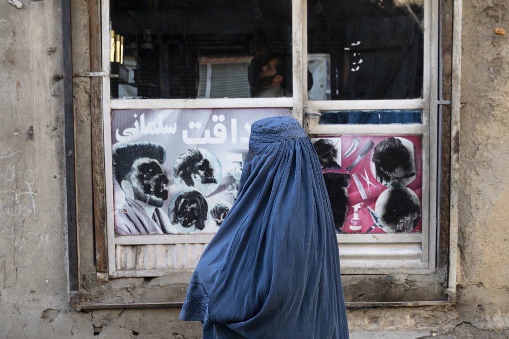 یک زن برقع پوش افغانستانی در ۳۱ ژانویه۲۰۲۴ از مقابل یک آرایشگاه با تصاویر مخدوش مردان در منطقه کوچ سنگ تراشی کابل عبور می‌کند.