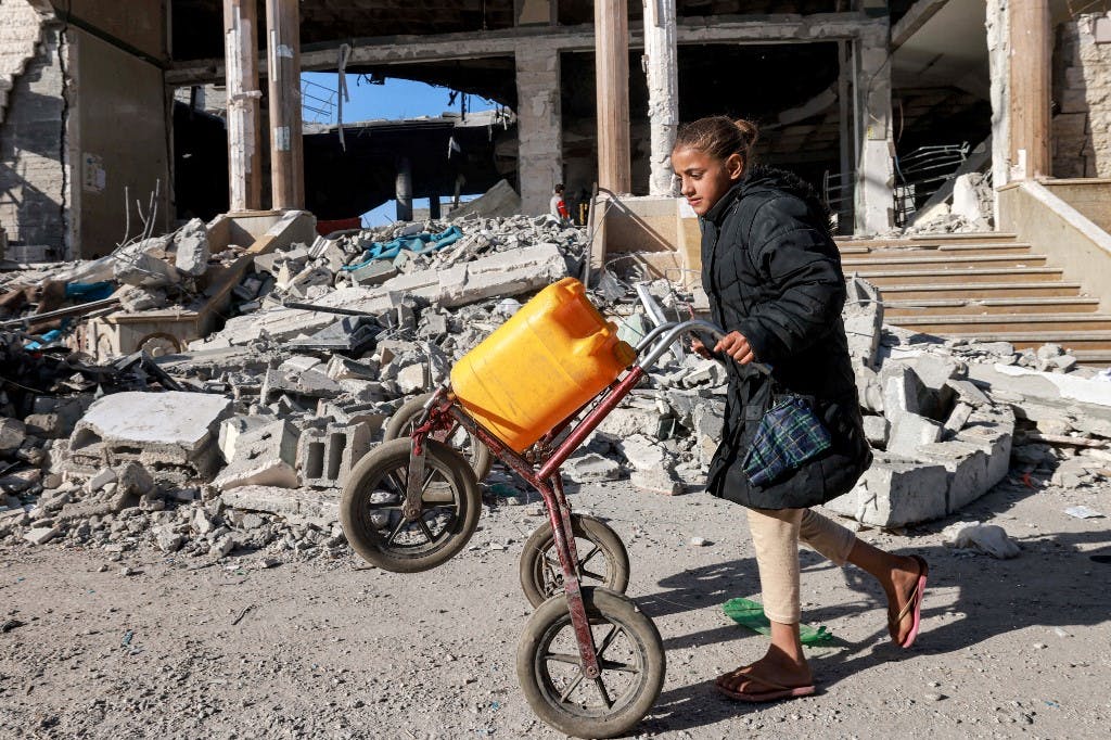 دختری در حالی که از کنار آوارهای ساختمانی که در جریان بمباران اسرائیل در رفح در جنوب نوار غزه در ۱۴ فوریه ۲۰۲۴، در بحبوحه درگیری‌های مداوم بین اسرائیل و حماس، ویران شد، گاری را هل می‌دهد.