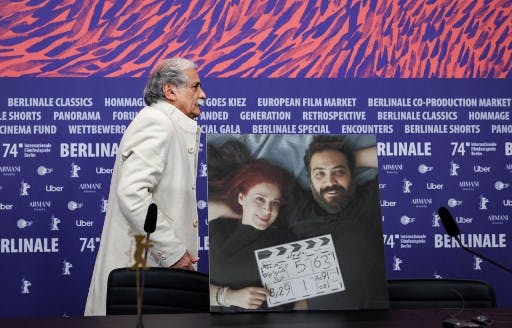 Actor Esmail Mehrabi walks past a photograph depicting Iranian actress and screenwriter Maryam Moghaddam (L) and Iranian film director and screenwriter Behtash Sanaeeha that is placed at their empty seats during a press conference for the film 'Keyke mahboobe man' (My favourite Cake) presented in competition during the 74th Berlinale, Europe's first major film festival of the year, in Berlin on February 16, 2024. The two Iranians said they have been barred from travelling to the Berlin film festival for their new movie's premiere for breaking one of their country's biggest taboos: showing a woman pursuing a "normal life". Maryam Moghaddam and Behtash Sanaeeha told AFP by video link from Tehran that they knew they were playing with fire with "My Favourite Cake", one of 20 films vying for the Golden Bear top prize. (Photo by Ronny HARTMANN / AFP)