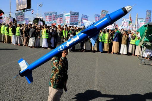 یک یمنی با لباس ارتشی که ماکت موشک بالیستیک آبی‌رنگ را روی دوش گرفته است