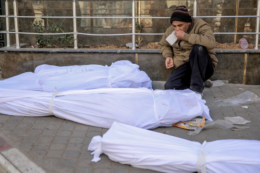 در مقابل بیمارستان شفا غزه یک مرد بر روی زمین نشسته و سه جنازه کفن شده مقابل او قرار دارند. ۲۹ فوریه ۲۰۲۴