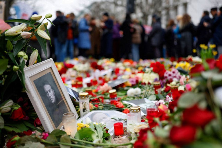 در تصویر انبوهی شمع و گل بر روی زمین دیده می‌شود و روی آن‌ها عکس سیاه و سفید آلکسی ناوالنی قرار دارد. در پسزمینه تصویر مردم ایستاده‌اند.