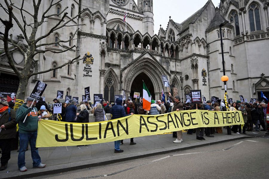 حامیان جولیان آسانژ در حالی‌که تصاویر او را در دست دارند در مقابل دادگاه جزای لندن جمع شده‌اند. آن‌ها یک پلاکارد بزرگ که روی آن نوشته شده «جولیان آسانژ یک قهرمان است» جلوی جمعیت گرفته‌اند. یک پرچم ایرلند نیز در میان جمعیت دیده می‌شود.