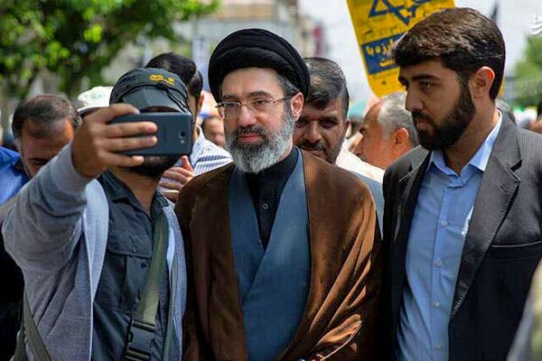 مجتبی خامنه‌ای، فرزند علی خامنه‌ای در میان دو نفر قرار دارد که یکی از آن‌ها با او در حال سلفی گرفتن است.