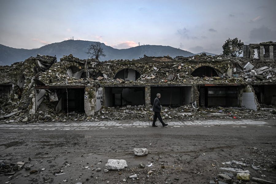 مرد سالمندی در کنار ساختمان ویران‌شده در شهر انتاکیه واقع در استان ختای قدم می‌زند. ویرانی ساختمان اثر باقی‌مانده از زلزله سال گذشته است. در افق آسمان رنگی است.