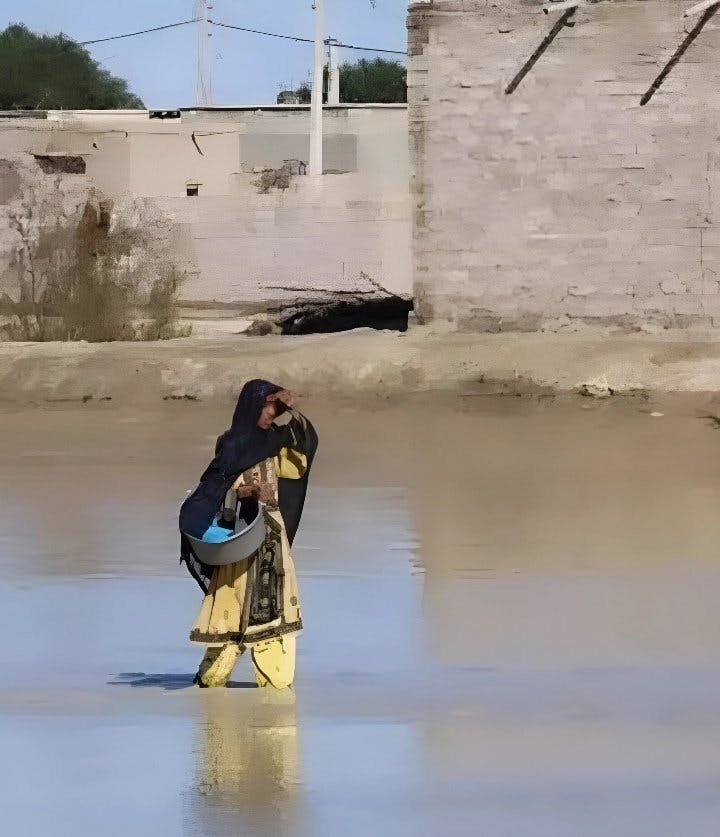 در یک خیابان آب‌گرفته یک زن بلوچ در حالی که تا زانو در آب است دیده می‌شود