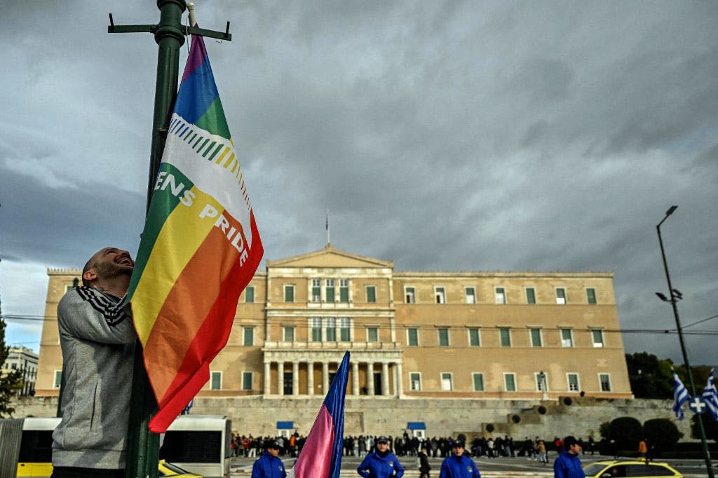یک نفر دارد پرچم جامعه ال‌جی‌بی‌تی‌کیو را در بیرون از ساختمان پارلمان یونان در آتن بر روی تیرکی آویزان می‌کند.