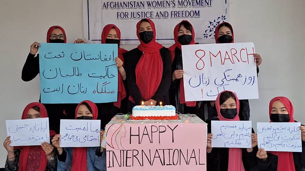 تصویری از زنان جنبش «زنان افغانستان برای عدالت و آزادی» - ۹ زن در تصویر دیده می‌شوند که ماسک به صورت دارند و پلاکاردهایی را با شعارهای مربوط به ۸ مارس در دست گرفته اند.
