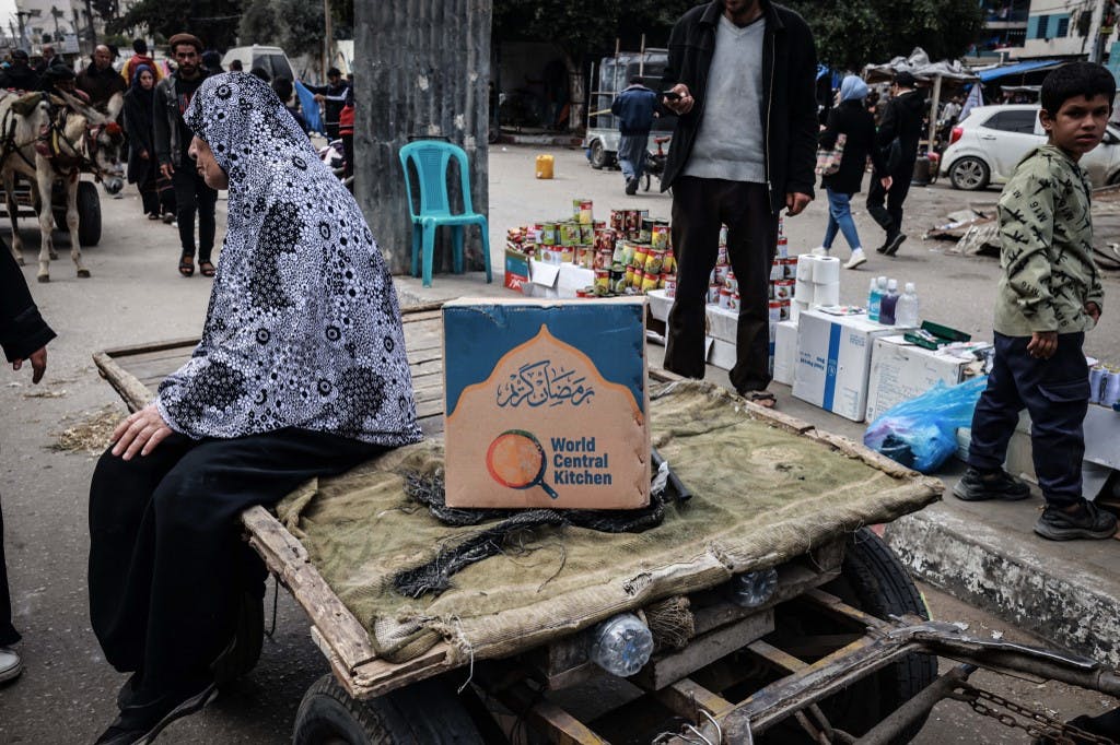 یک زن فلسطینی در یک بازار خیابانی موقت در رفح در جنوب نوار غزه، در کنار یک جعبه جیره غذایی که توسط سازمان خیریه آمریکایی World Central Kitchen ارائه شده است، روی گاری نشسته است. ۱۴ مارس ۲۰۲۴ (عکس از MOHAMMED ABED / AFP)