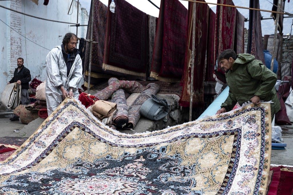 دو کارگر افغانستانی فرشی را گرفته اند و می کشند