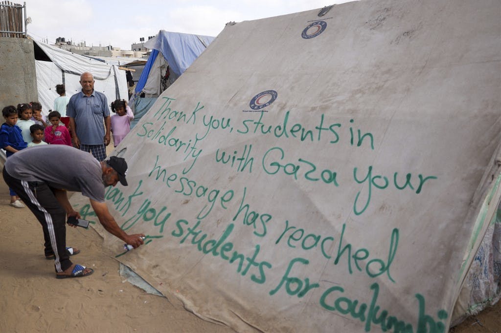 مردی در یک چادر در اردوگاه آوارگان فلسطینی در رفح در جنوب نوار غزه، پیام تشکری از دانشجویان آمریکایی در اعتراض به همبستگی با مردم غزه می نویسد. ۲۷آوریل ۲۰۲۴(عکس از خبرگزاری فرانسه)