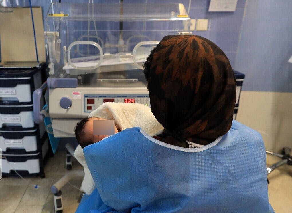 یک پرستار پشت به دوربین نوزادی را که تازه متولد شده در آغوش گرفته است