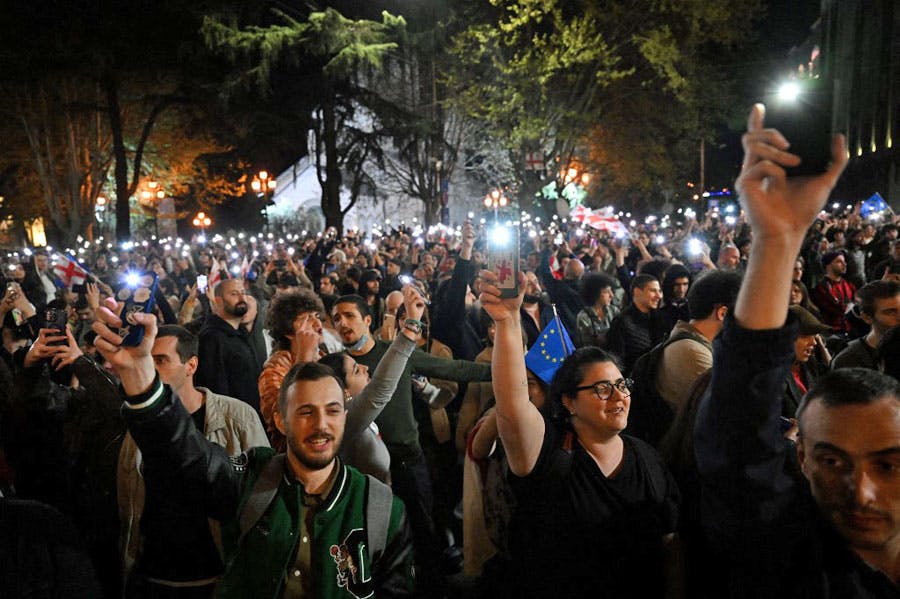 گروهی زیادی از مردم معترض تفلیس در هوای تاریک شب چراغ‌ تلفن‌های دستی خود را روشن کرده و تلفن‌ها را در دستان خود بالا گرفته‌اند. در میان آن‌ها پرچم‌های کوچک گرجستان و اتحادیه اروپا دیده می‌شود
