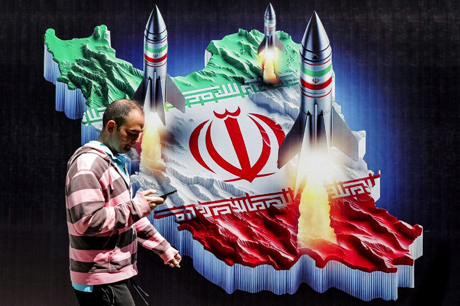 مردی در یکی از خیابان‌های تهران در حالی‌که با تلفن دستی خود مشغول است از کنار بنری می‌گذرد که در آن نقشه ایران با پرچم جمهوری اسلامی و سه موشک روی آن دیده می‌شود.
