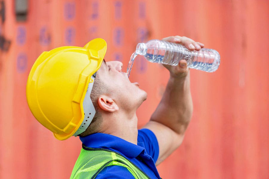 یک کارگر با کلاه حفاظتی در حال نوشیدن آب است.