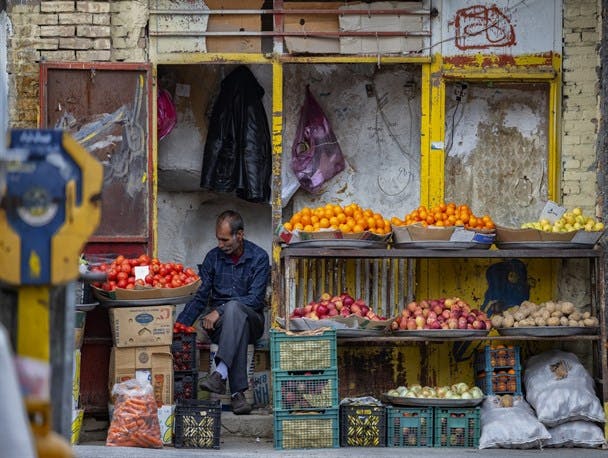 یک میوه فروش در مغازه‌ای مخروبه بدون مشتری نشسته است.