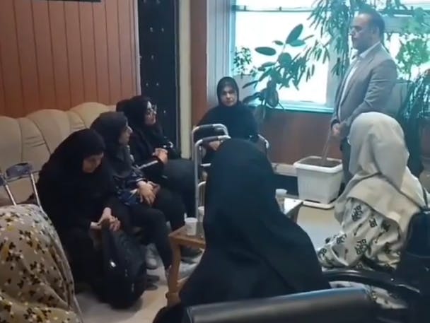 تصویر هفت زن را نشان می‌دهد که دورتادور اتاق نشسته‌اند و در گوشه‌ی تصویر، مردی که نایب رئیس شورای شهر کرج است ایستاده