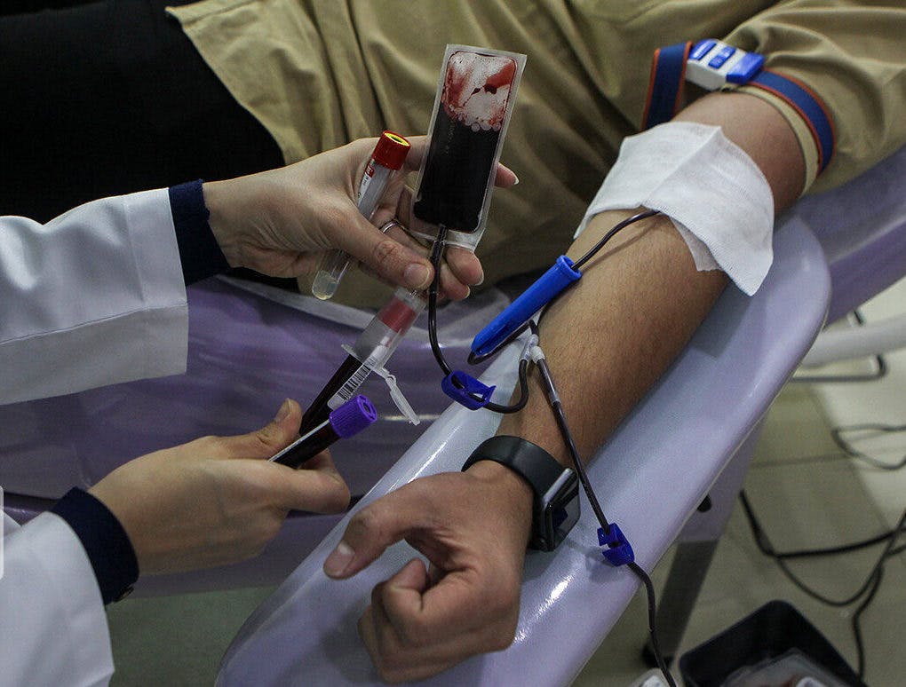 یک زن پرستار در حال تنظیم سرم خون به یک مرد روی تخت بیمارستان
