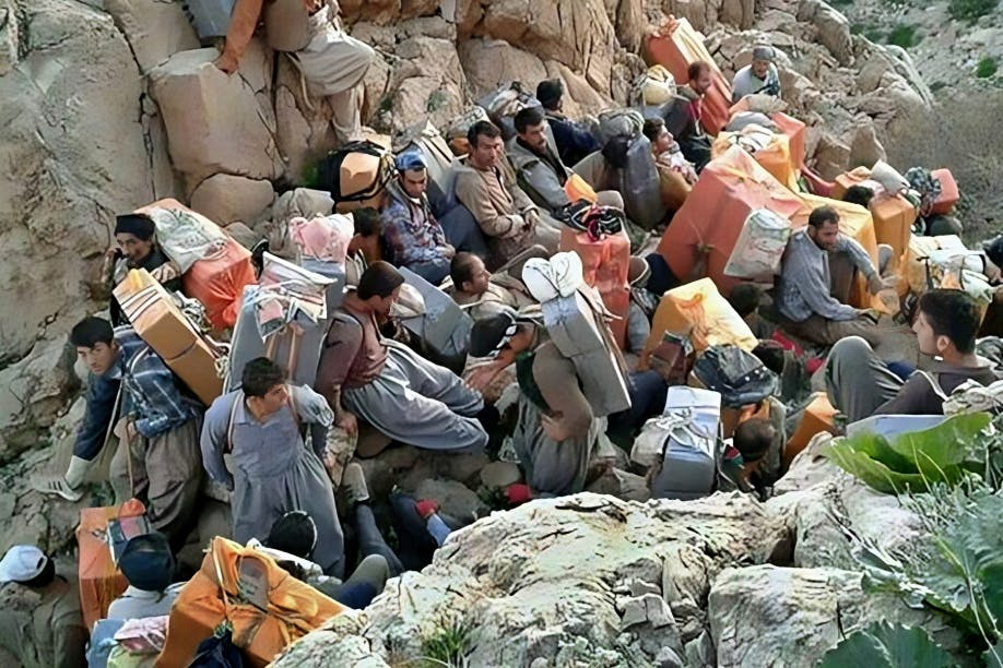گروهی از کولبران در کوهسار استراحت می‌کنند. آن‌ها با بارهای خود کنار هم نشسته‌اند.