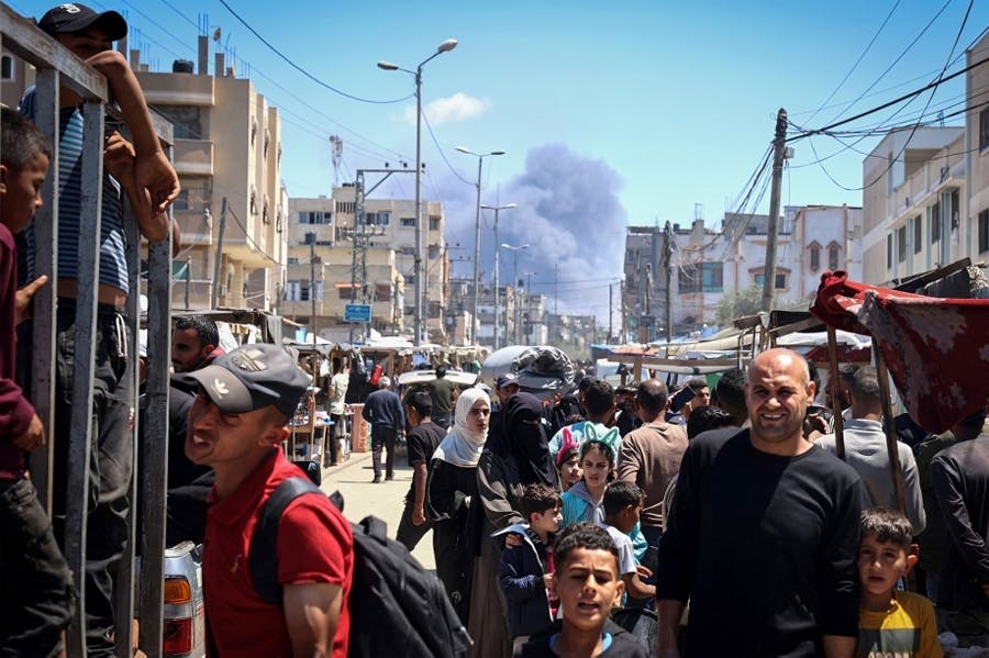تصویر یک خیابان مملو از جمعیت را در رفح نشان می‌دهد. در پسزمینه تصویر دود ناشی از بمباران‌ها به آسمان بلند شده است.