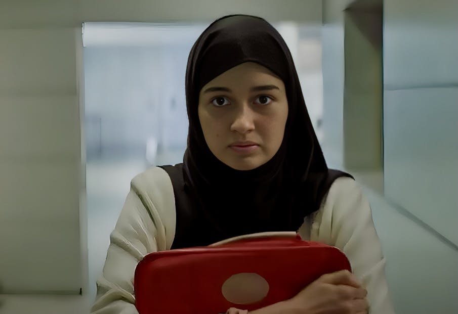 یک دختر نوجوان با حجاب اسلامی در فرودگاه چمدان قرمزی را دبر سینه خود می‌فشرد