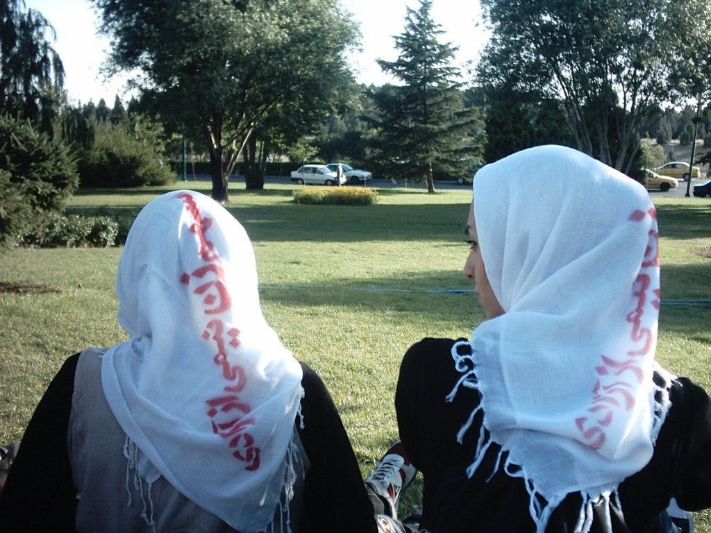 دو زن نشسته بر یک چمن سبز با روسری سفید که بر آن با قرمز نوشته شده سهم زنان نیمی از آزادی