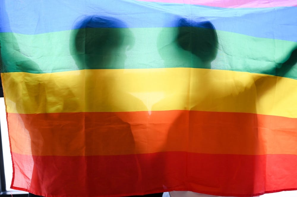 تصویر تزئینی از شاتر استاک سایه دو نفر را در پس پرچم رنگین‌کمان نشان می‌دهد که نماد جامعه کوئیر است.