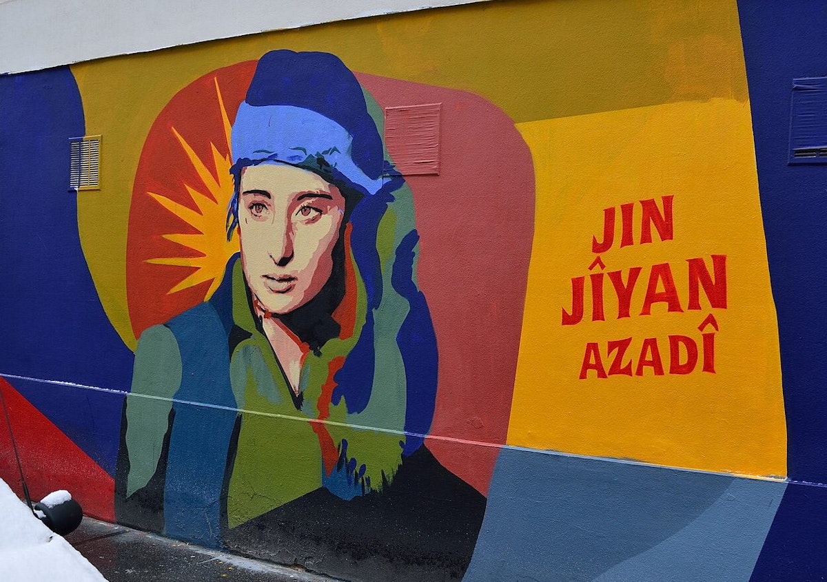 یک دیوارنگاری رنگارنگ که در آن تصویر یک زن مبارز کرد کناز شعار ژن ژیان ئازادی دیده می‌شود