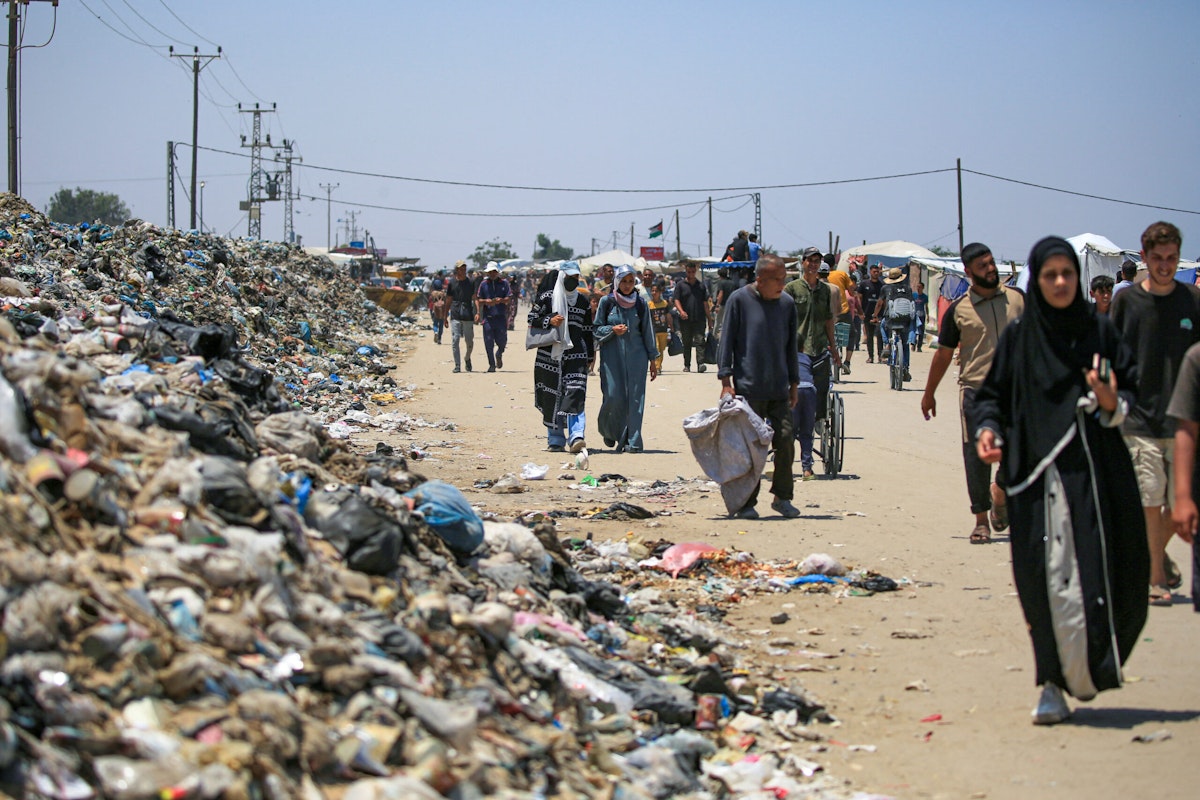آوارگان فلسطینی از کنار تلی از زباله حرکت می‌کنند