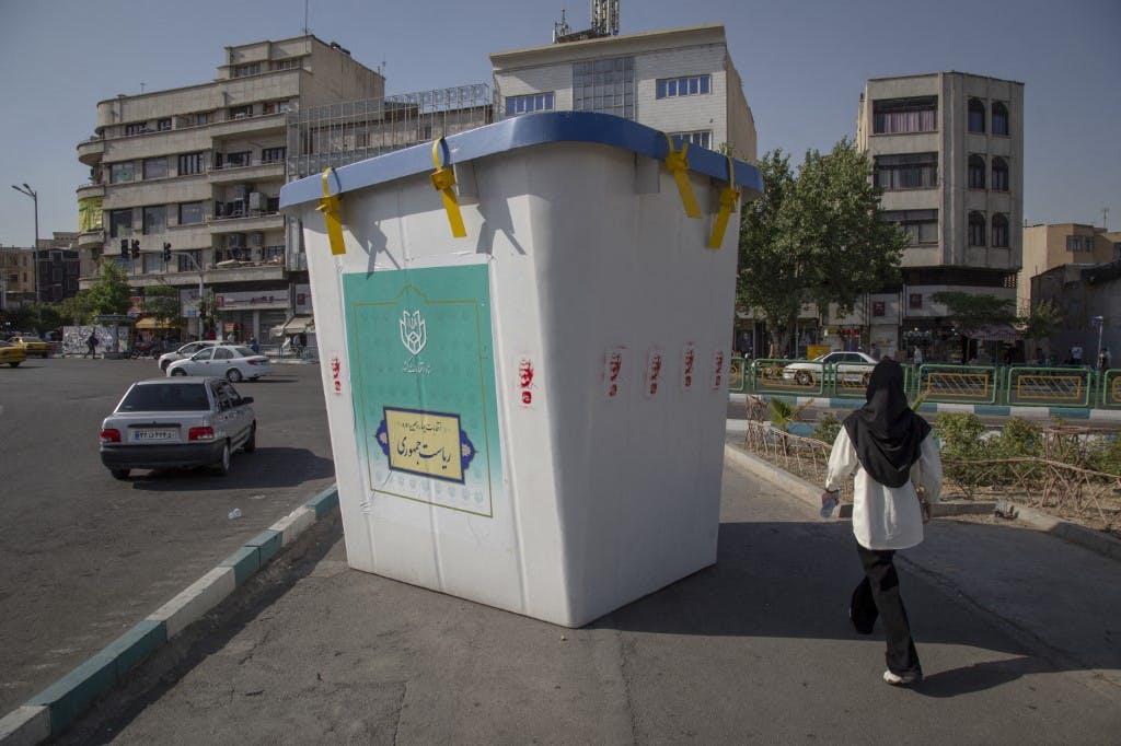 زنی در پیاده‌رو خیابانی در تهران از کنار یک صندوق ررای تبلیغاتی که دو برابر او ارتفاع دارد رد می‌شود