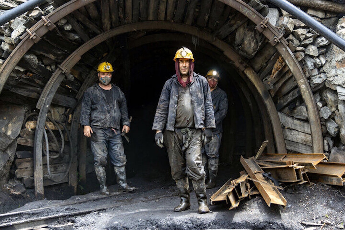 سه کارگر معدن در ورودی یک تونل با لباس کار ایستاده اند.