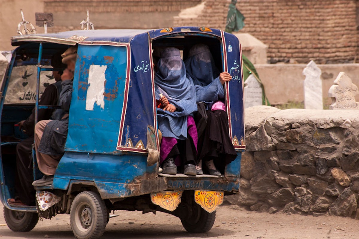 دو زن افغان در پشت یک تاکسی سه‌چرخه نشسته‌اند و به بیرون نگاه می‌کنند. آن‌ها سر تا پای خود را پوشانده‌اند.