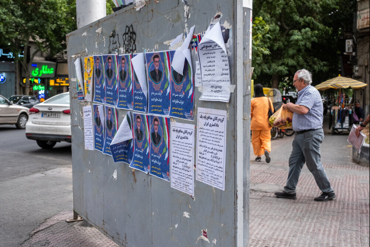 پوسترهای کاندیداهای ۱۴۰۳ بر دیوار خیابانی در تهران. مردی در حاشیه قدم می‌زند