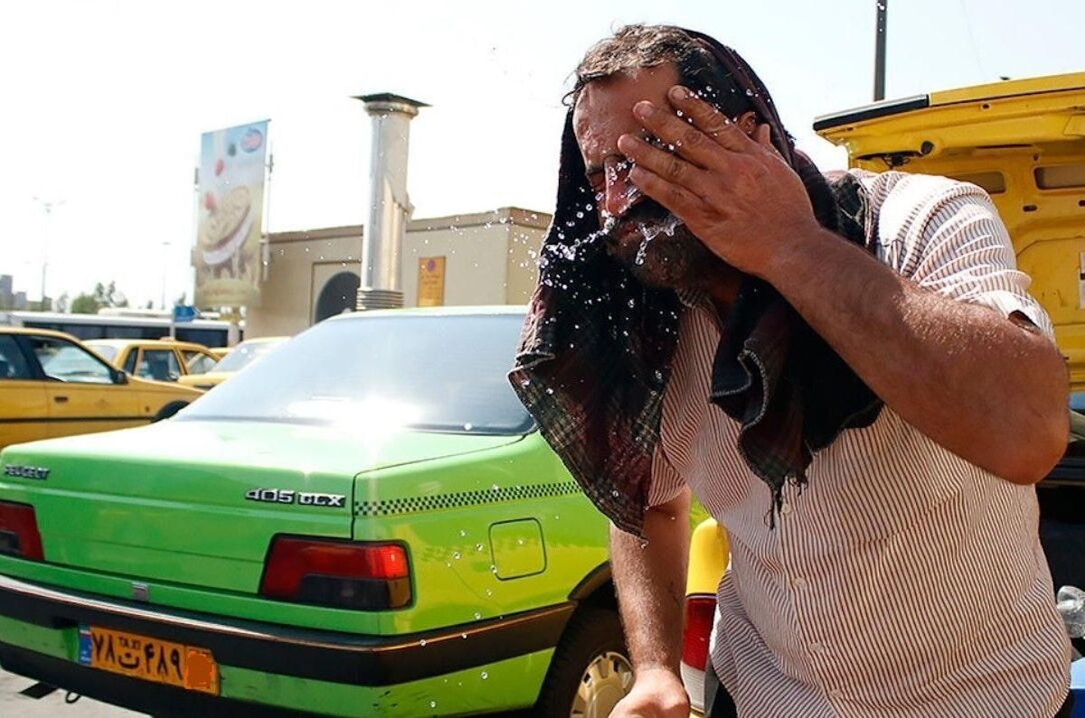 تصویری از یک مرد که در گرما آب روی خدش می ریزد و در پس زمینه یک ماشین سبز