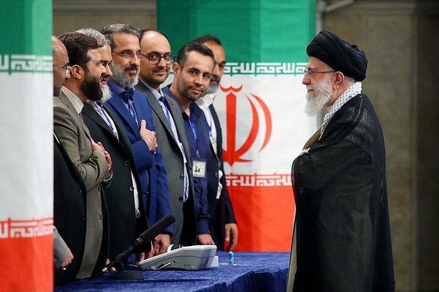 علی خامنه‌ای روبه‌روی عده‌ای از دست‌اندرکاران انتخابات ریاست جمهوری ایستاده و آ‌ن‌ها دست به سینه به او نگاه می‌کنند.