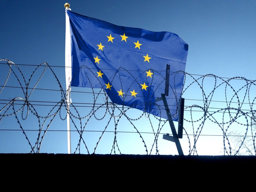 پرچم اتحادیه اروپا در آسمان ابری بیرون از سیم خاردار زندان آویزان است.