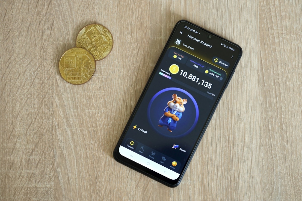 تصویر یک گوشی موبایل با تصویر بازی همستر کامبت، و دو سکه در کنار گوشی