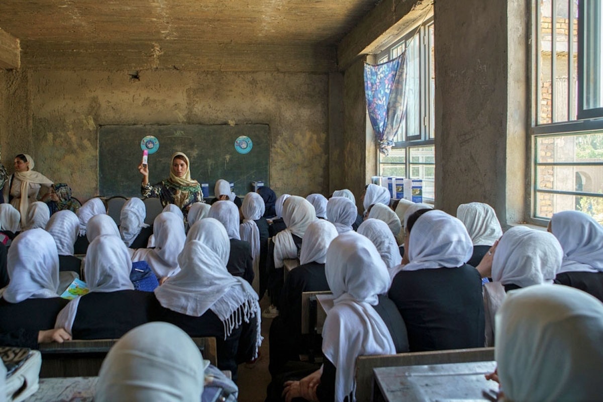 در تصویر کلاس درس یک مدرسه دخترانه در افغانستانِ پیش از حکومت طالبان نشان داده می‌شود که در آن دختران با روسری‌های سفید پشت به ما نشسته‌اند و در روبه‌رو یک معلم زن در حال آموزش به آن‌هاست.