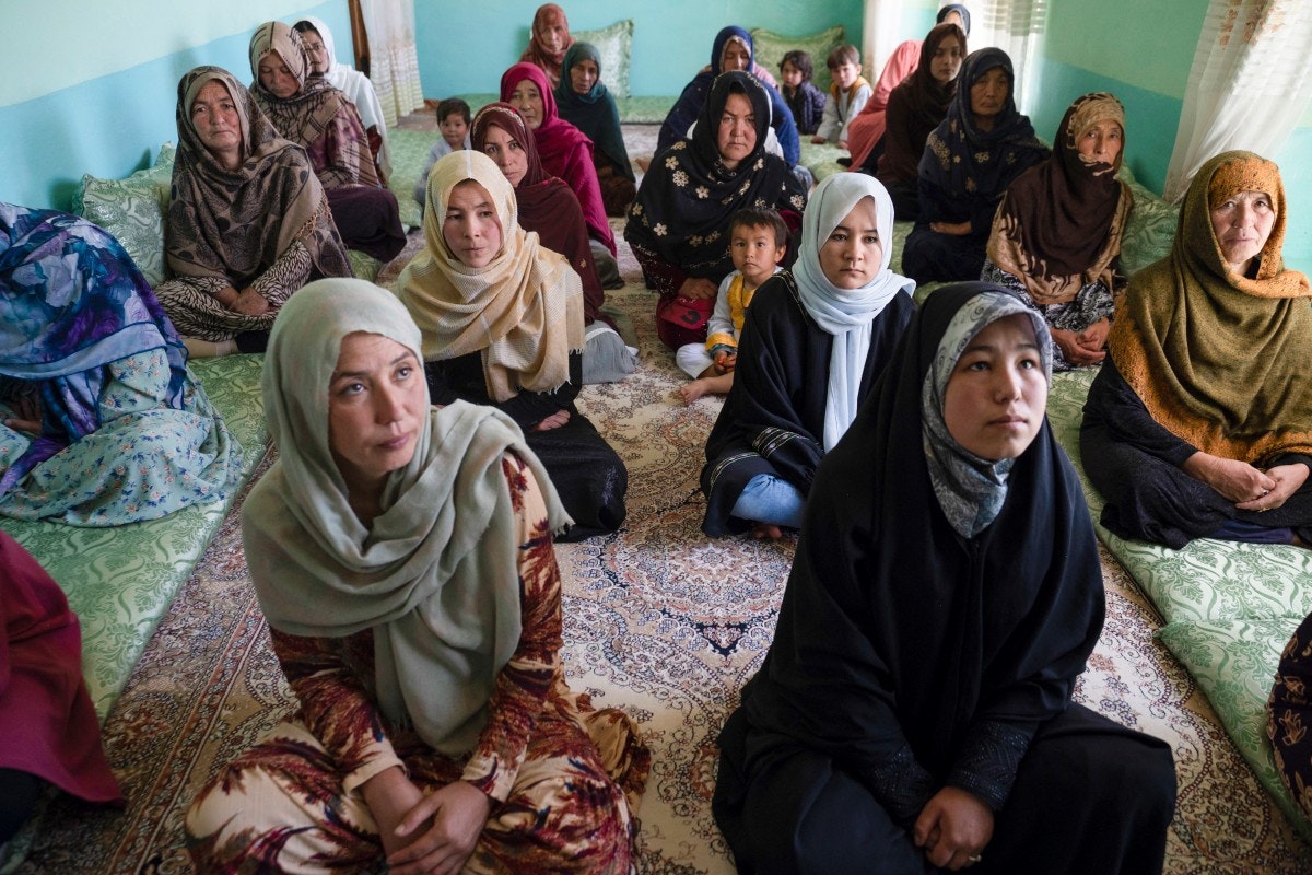بیش از ده زن افغانستانی از سنین مختلف در یک کلاس روی زمین نشسته‌اند.