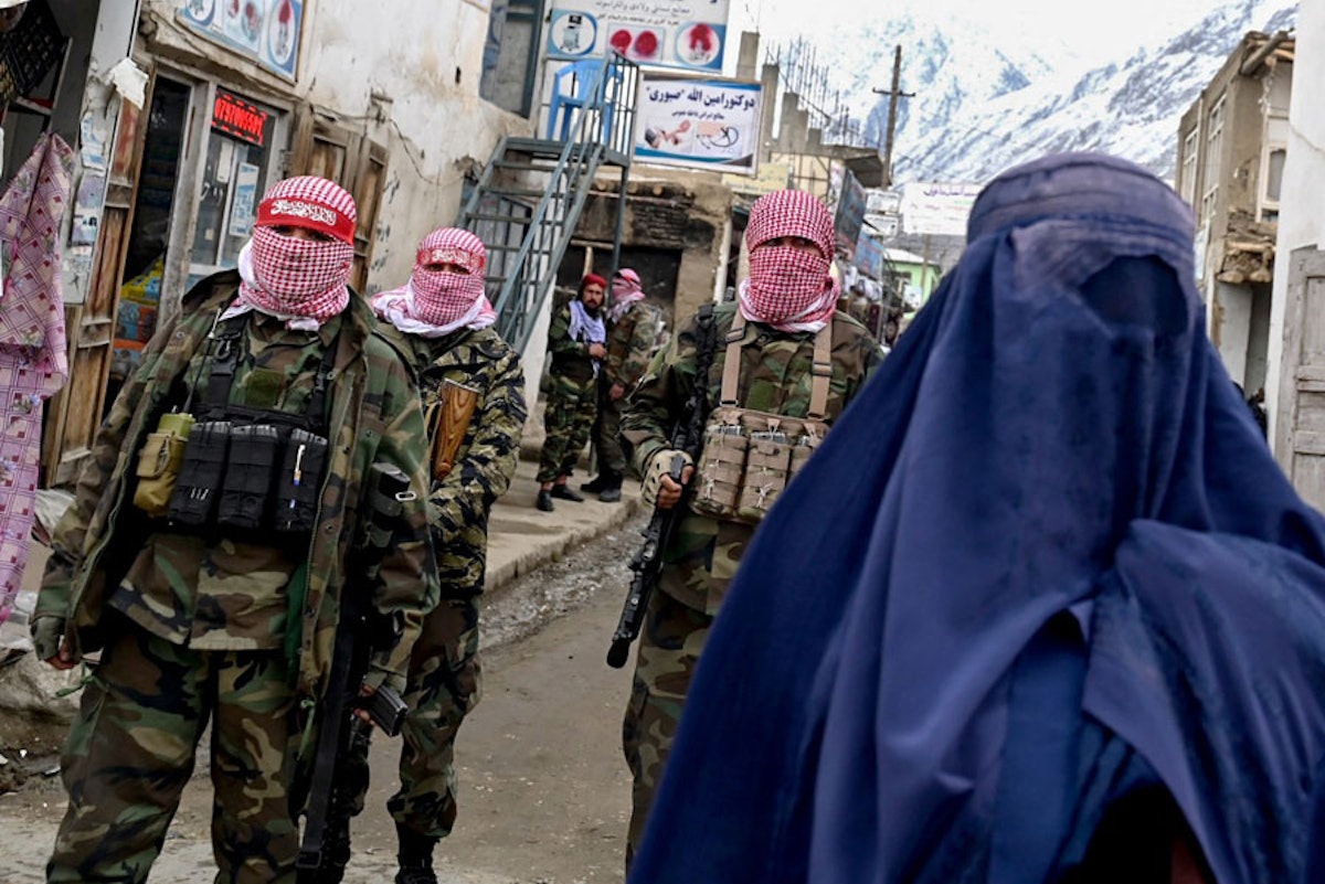 سه مأمور طالبان با دستمال چفیه قرمز و سفید چهره‌های خود را پوشانده‌اند و در کنار یک زن که سر تا پای خود را با برقع پوشانده است راه می‌روند. در پسزمیه تصویر دو مأمور دیگر طالبان و کوهستان برفی دیده می‌شوند.